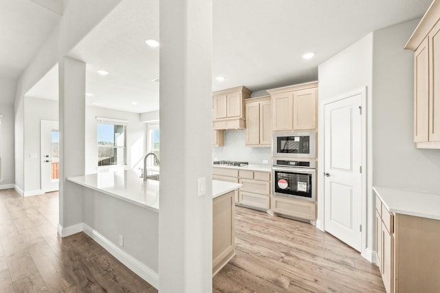 kitchen featuring light hardwood / wood-style floors, oven, black microwave, light brown cabinetry, and decorative backsplash