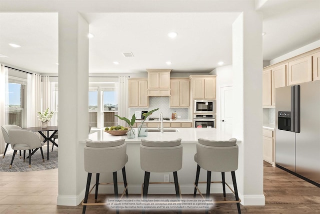 kitchen featuring wood-type flooring, a kitchen breakfast bar, stainless steel appliances, decorative backsplash, and sink