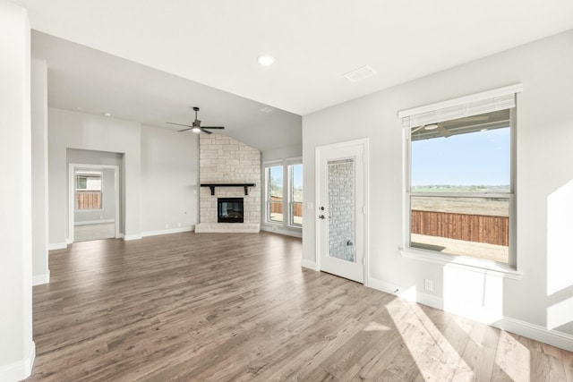 unfurnished living room featuring ceiling fan, vaulted ceiling, a stone fireplace, and wood-type flooring