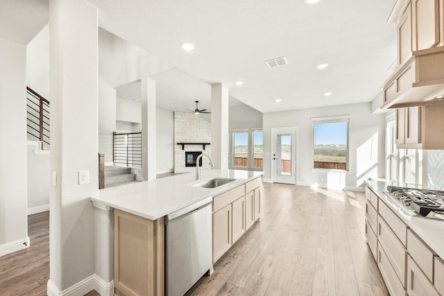 kitchen featuring light hardwood / wood-style flooring, light brown cabinetry, stainless steel appliances, sink, and a brick fireplace