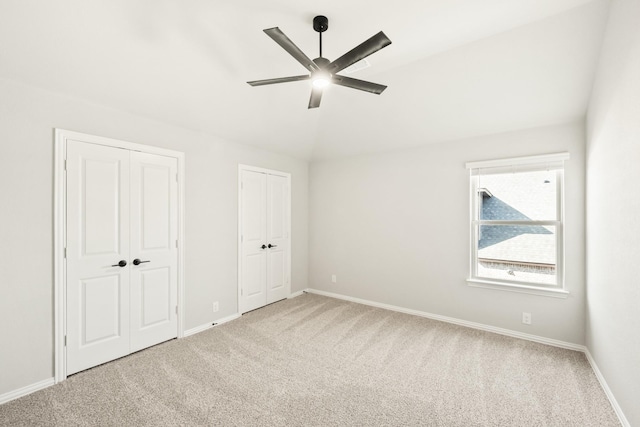 unfurnished bedroom featuring lofted ceiling, carpet flooring, ceiling fan, and multiple closets