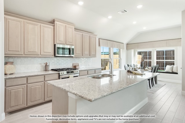 kitchen featuring appliances with stainless steel finishes, vaulted ceiling, light stone counters, a center island with sink, and sink