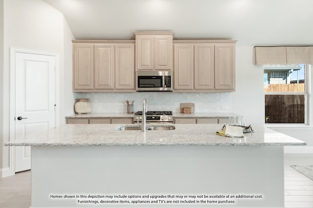 kitchen with light stone countertops, light wood-type flooring, backsplash, and a kitchen island with sink