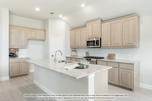 kitchen with appliances with stainless steel finishes, an island with sink, tasteful backsplash, light stone countertops, and sink