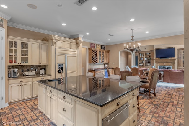 kitchen with a chandelier, sink, cream cabinetry, a center island with sink, and paneled fridge