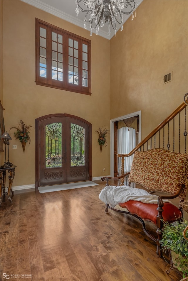 foyer with a towering ceiling, ornamental molding, a chandelier, and hardwood / wood-style floors