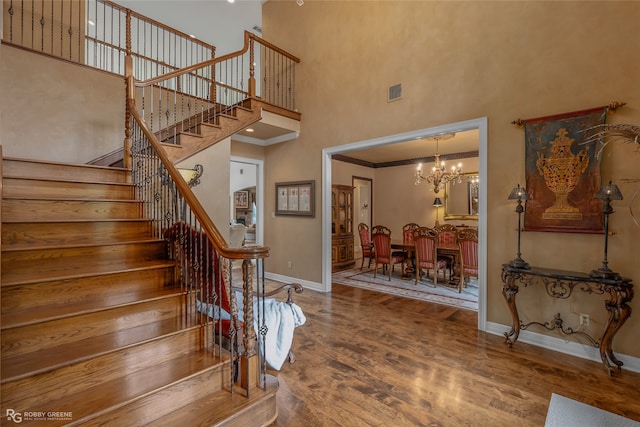 stairs with hardwood / wood-style flooring, a towering ceiling, a chandelier, and crown molding