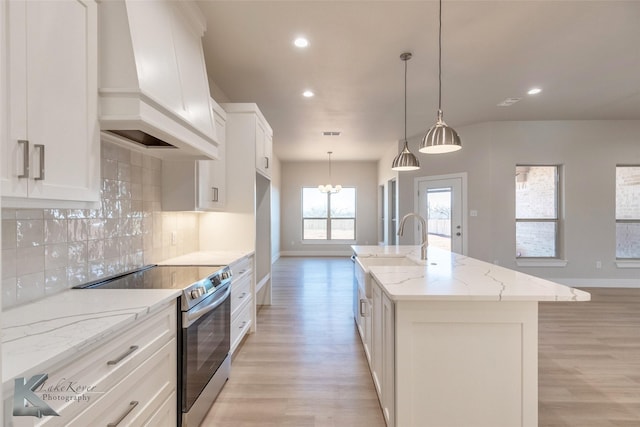 kitchen featuring light wood finished floors, tasteful backsplash, an island with sink, custom range hood, and stainless steel range with electric cooktop