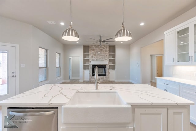 kitchen with light stone counters, open floor plan, a stone fireplace, stainless steel dishwasher, and a sink