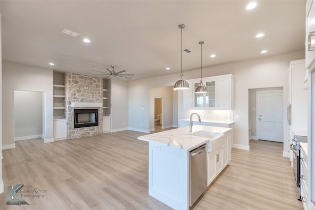 kitchen featuring white cabinetry, stainless steel appliances, a sink, and a stone fireplace