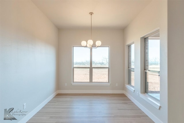 unfurnished dining area with an inviting chandelier, baseboards, and light wood-style floors