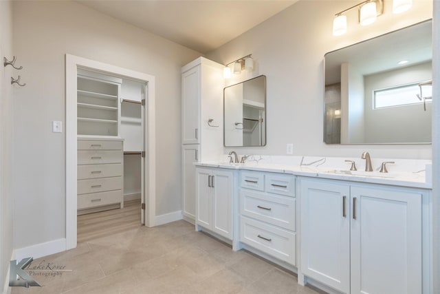 bathroom featuring double vanity, a sink, a walk in closet, and baseboards