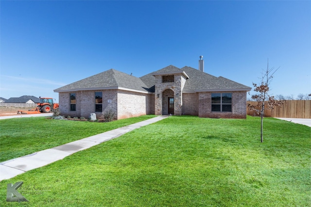 view of front of property featuring a shingled roof, fence, a front lawn, and brick siding