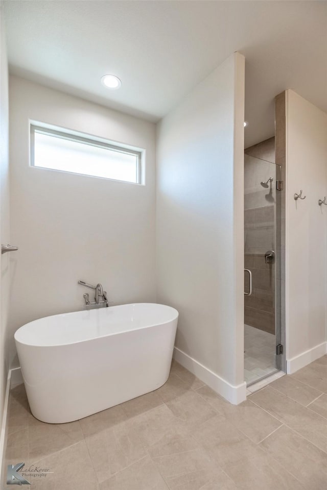 full bath featuring a freestanding tub, a shower stall, baseboards, and tile patterned floors