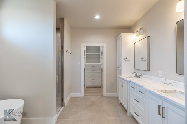 bathroom featuring double vanity, a soaking tub, a spacious closet, a stall shower, and a sink