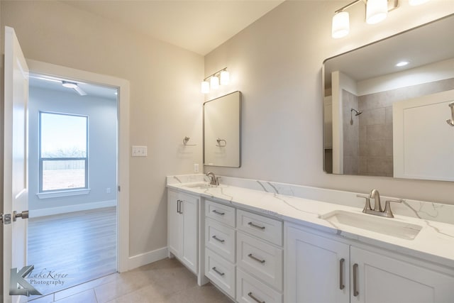 bathroom featuring double vanity, baseboards, a sink, and tiled shower