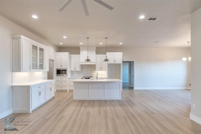 kitchen featuring stainless steel microwave, visible vents, decorative backsplash, white cabinets, and light wood-type flooring