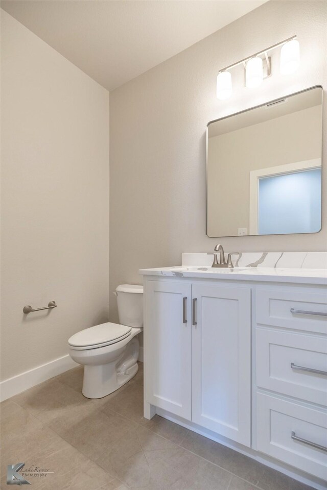 half bath with baseboards, vanity, toilet, and tile patterned floors