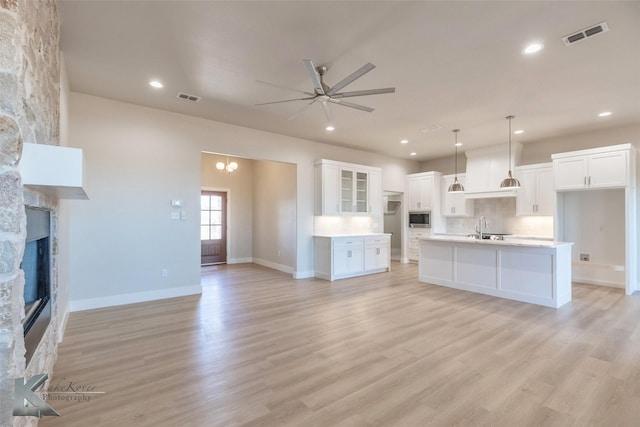 unfurnished living room with light wood-style floors, visible vents, and a stone fireplace