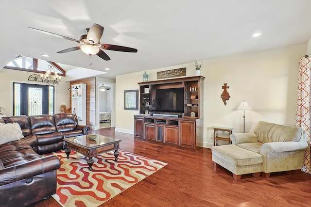 living room featuring ceiling fan with notable chandelier, dark wood-type flooring, and vaulted ceiling