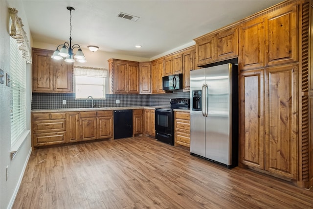 kitchen featuring sink, black appliances, decorative light fixtures, light hardwood / wood-style flooring, and decorative backsplash