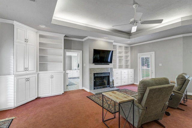 carpeted living room featuring ornamental molding, a raised ceiling, ceiling fan, and a tile fireplace