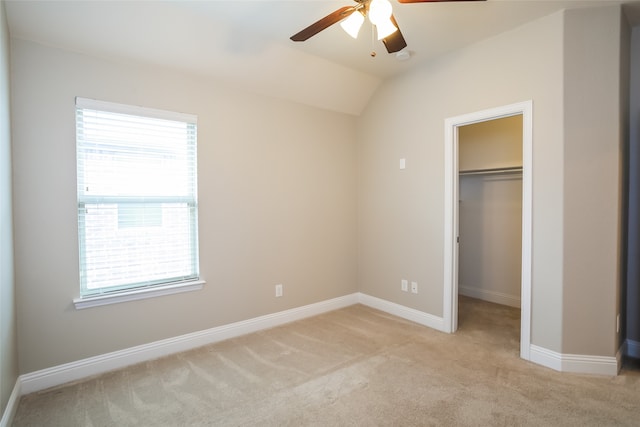 unfurnished bedroom featuring vaulted ceiling, a spacious closet, a closet, ceiling fan, and light colored carpet