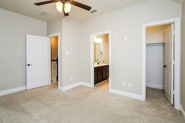 unfurnished bedroom featuring a closet, light colored carpet, a walk in closet, ensuite bathroom, and ceiling fan