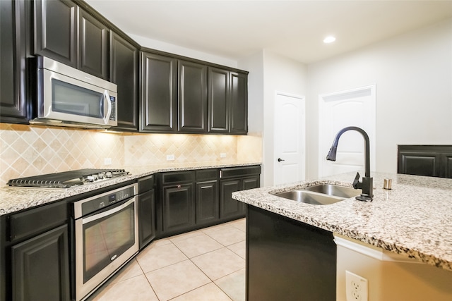 kitchen with light tile patterned floors, stainless steel appliances, sink, and light stone countertops