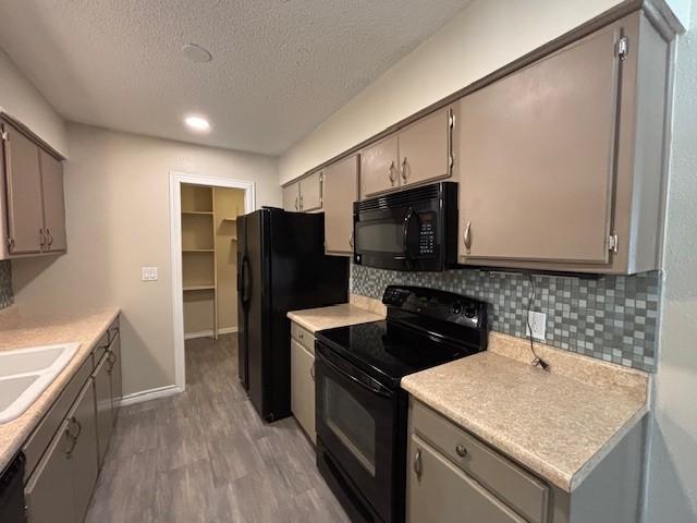 kitchen featuring light wood finished floors, backsplash, gray cabinetry, black appliances, and a sink