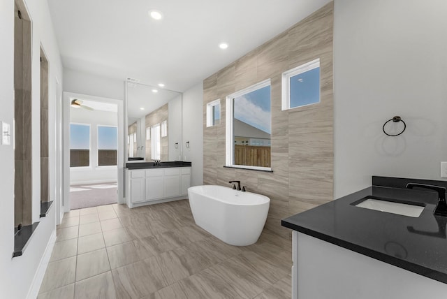 bathroom featuring tile patterned floors, vanity, ceiling fan, a bath, and tile walls