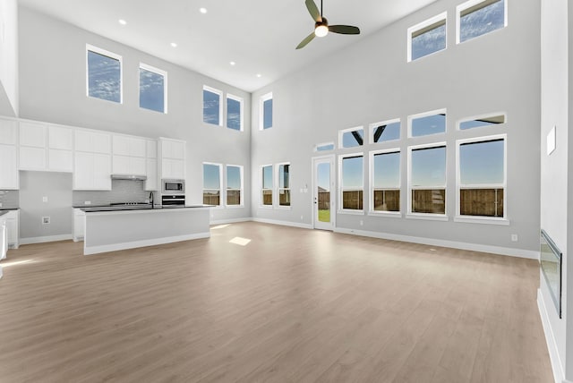 unfurnished living room featuring plenty of natural light, light wood-style floors, ceiling fan, and baseboards