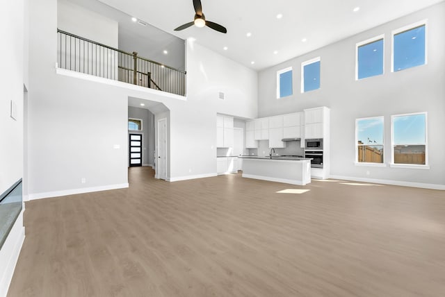 unfurnished living room featuring ceiling fan, a towering ceiling, sink, and light hardwood / wood-style flooring