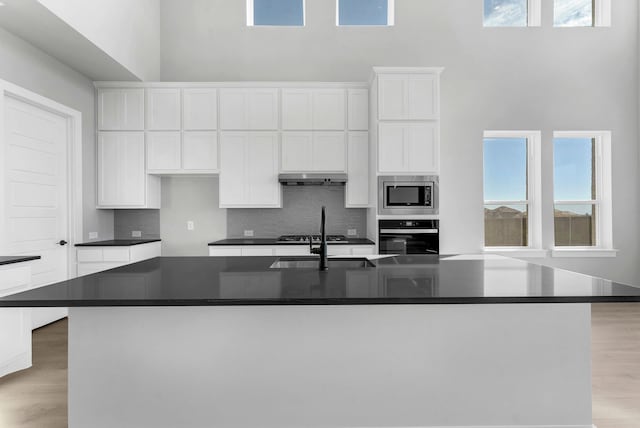 kitchen featuring backsplash, white cabinetry, a center island with sink, and stainless steel appliances