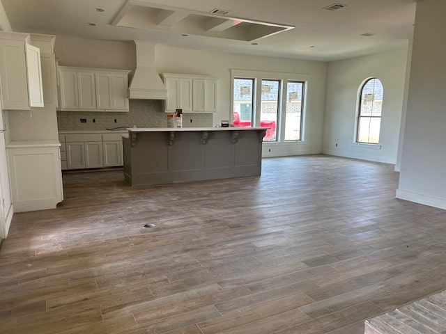 kitchen featuring white cabinets, a center island with sink, custom range hood, a breakfast bar area, and light wood-type flooring