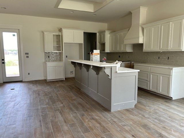 kitchen with light wood-type flooring, custom range hood, tasteful backsplash, and a center island