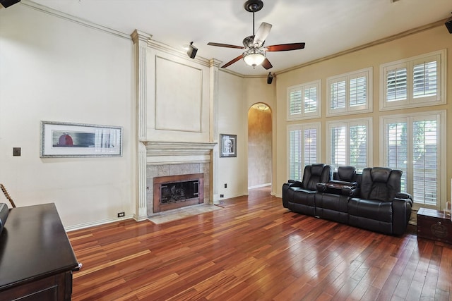 living room featuring ceiling fan, dark hardwood / wood-style floors, crown molding, and a tile fireplace