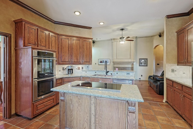 kitchen with appliances with stainless steel finishes, backsplash, crown molding, ceiling fan, and a center island with sink