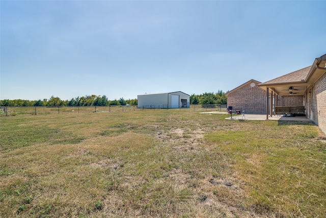 view of yard with a patio, an outdoor structure, ceiling fan, and a rural view