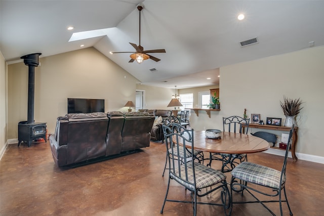 dining area with ceiling fan, vaulted ceiling with skylight, and a wood stove