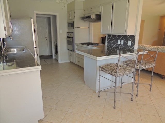 kitchen featuring a breakfast bar, washer / clothes dryer, range hood, kitchen peninsula, and appliances with stainless steel finishes