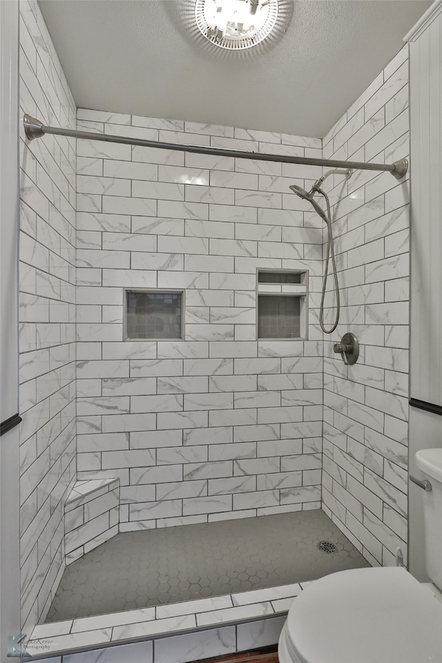 bathroom with a tile shower, a textured ceiling, and toilet