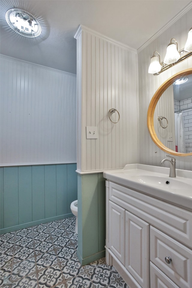 bathroom featuring wooden walls, ornamental molding, vanity, and toilet