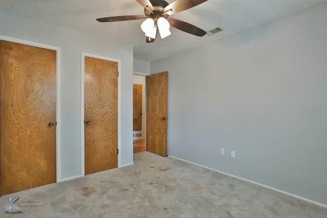 unfurnished bedroom with a textured ceiling, ceiling fan, light colored carpet, and multiple closets