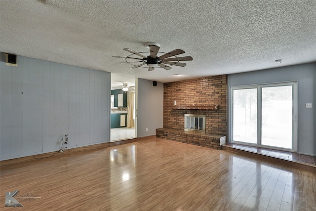 unfurnished living room featuring a brick fireplace, ceiling fan, hardwood / wood-style flooring, and a textured ceiling