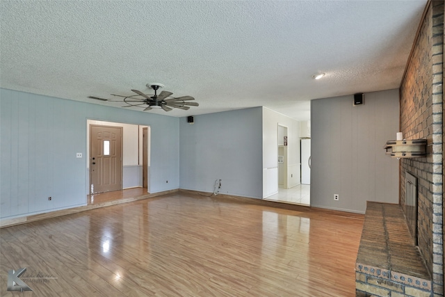 unfurnished living room with light wood-type flooring, a textured ceiling, a fireplace, and ceiling fan