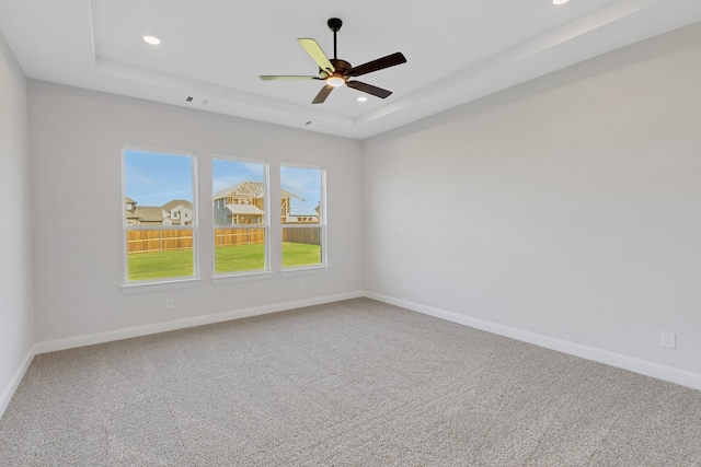 empty room featuring a raised ceiling, carpet floors, and ceiling fan