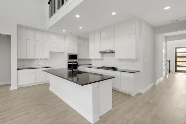 kitchen with built in microwave, stainless steel gas stovetop, a kitchen island with sink, and white cabinets