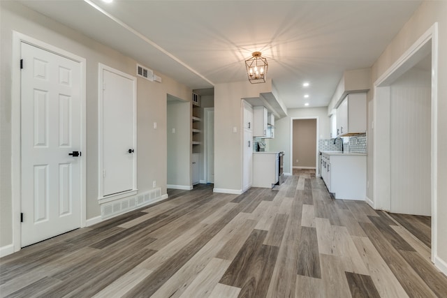 interior space with white cabinets, sink, light hardwood / wood-style flooring, backsplash, and stainless steel range oven