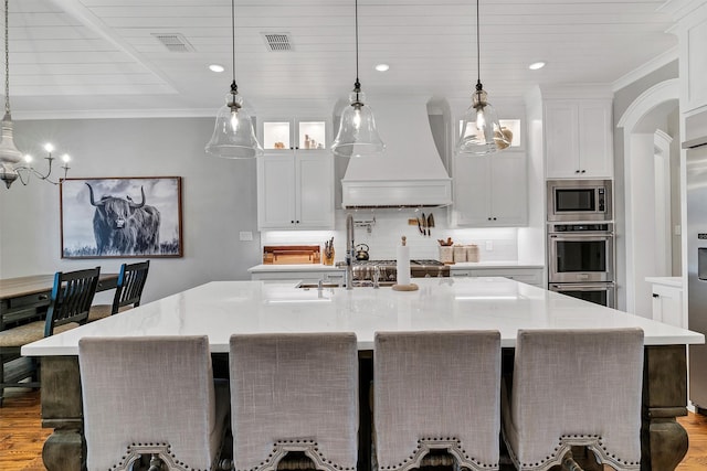 kitchen featuring white cabinets, custom exhaust hood, hanging light fixtures, and a large island with sink